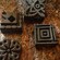 Four square shaped artifacts with geometric and floral designs sit on a table